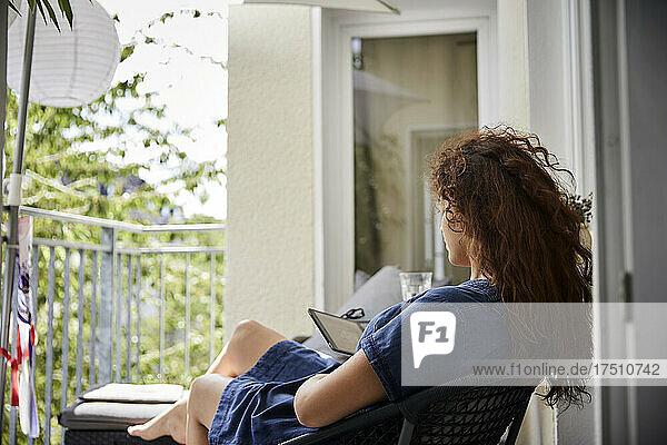 Woman reading from e-reader while sitting on chair at balcony