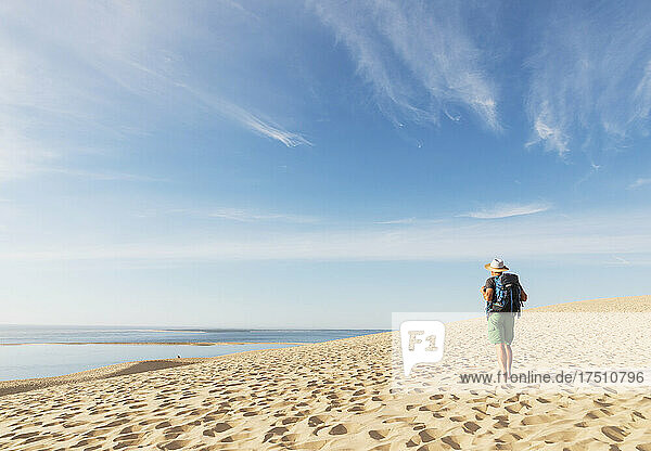 Senior man with backpack looking at Atlantic ocean while standing on beach  Dune of Pilat  Nouvelle-Aquitaine  France