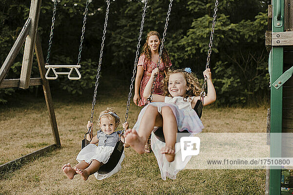Happy girls on a swing with mother in background