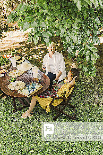 Cheerful mother and daughter enjoying picnic while sitting in yard