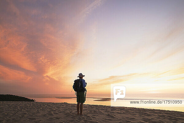 Senior man with backpack looking at Atlantic ocean against sky during sunset  Dune of Pilat  Nouvelle-Aquitaine  France