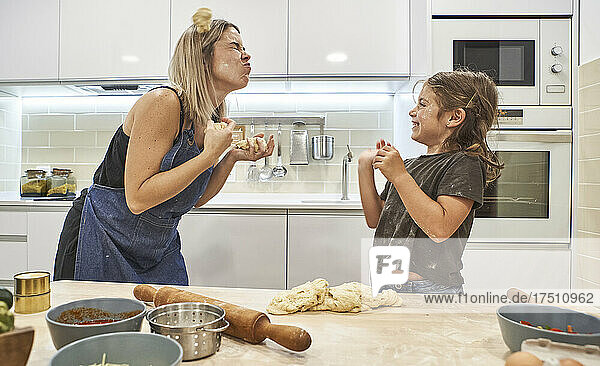 Mother and daughter playing with pizza dough in kitchen at home