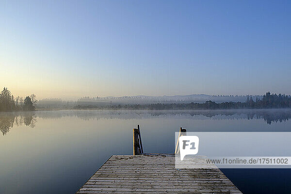 Jetty on shore of Kirchsee lake at foggy dawn