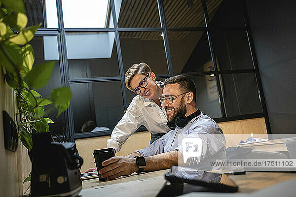 Lächelnde Unternehmer und Unternehmerinnen schauen auf den Laptop  während sie im Büro eine Strategie planen