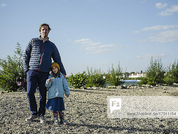 Father with daughter standing on land against sky during sunny day
