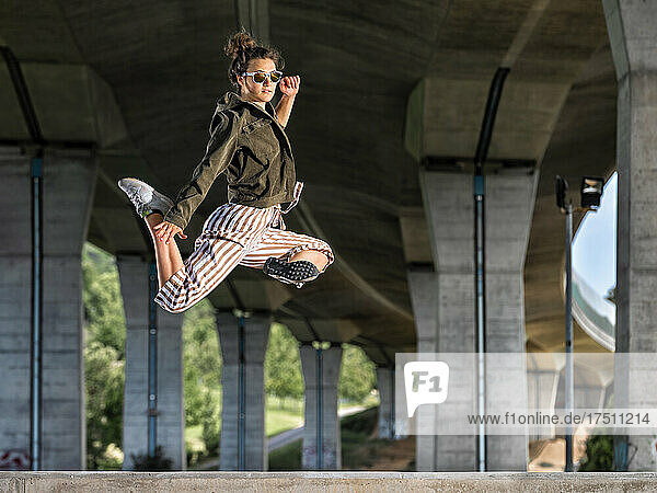 Young womann doing acrobatics and jumping under bridge