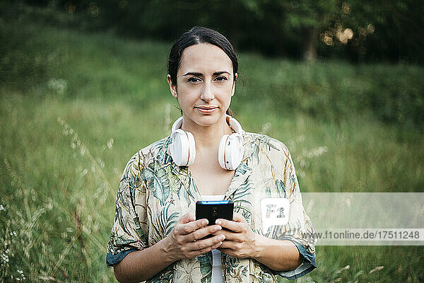 Woman standing with smart phone and headphones in public park