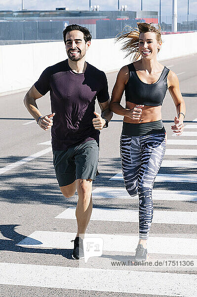 Smiling couple running on street in city during sunny day