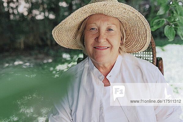 Close-up of smiling senior woman wearing hat sitting on chair in yard