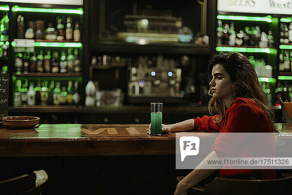 Thoughtful woman with drink on bar counter sitting in restaurant