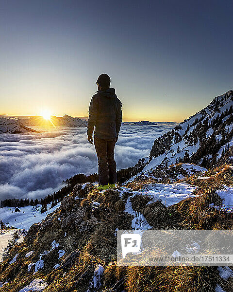 Man admiring sunrise over mountain valley shrouded in fog