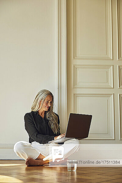 Lächelnde Frau benutzt Laptop  während sie zu Hause auf dem Boden sitzt