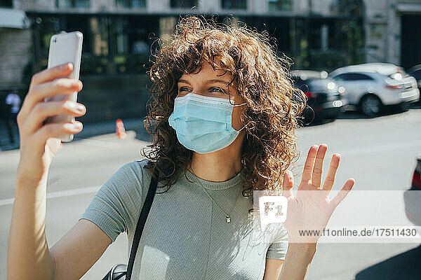 Woman wearing protective mask and using smartphone in city
