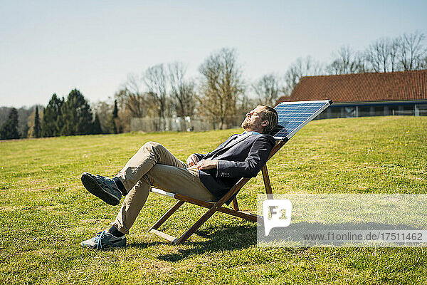 Businessman relaxing on chair with solar panel at park during sunny day