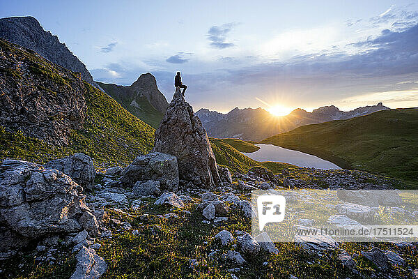 Wanderer sitzt auf einem Felsen bei Sonnenuntergang am Rappensee  Bayern  Deutschland
