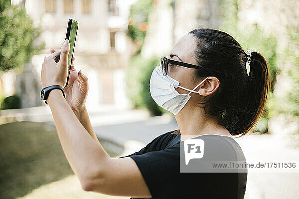 Frau trägt Schutzmaske und macht ein Foto mit ihrem Smartphone