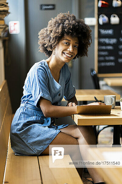 Glückliche junge Frau schreibt am Tisch im Café in ein Buch