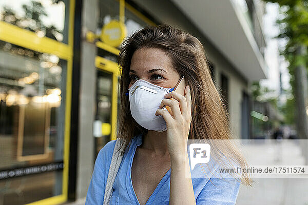 Close-up of young woman wearing mask talking over smart phone in city