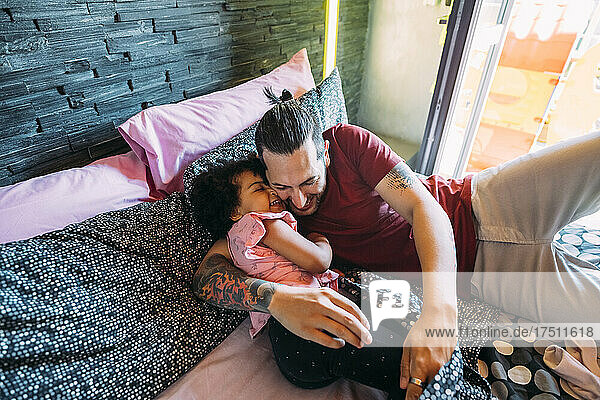 Playful father and daughter lying on bed at home