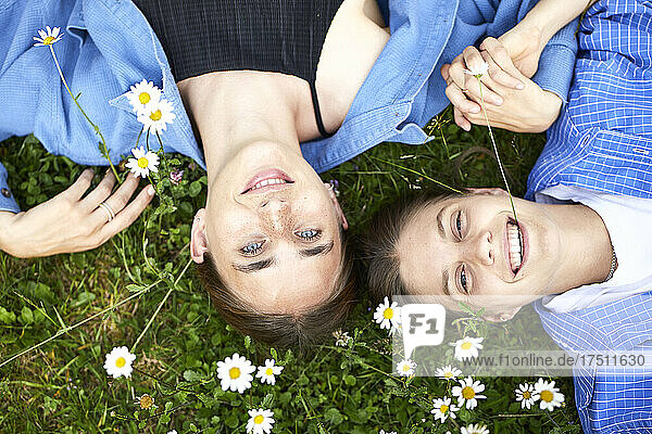 Close-up of smiling young friends lying on grassy land in garden