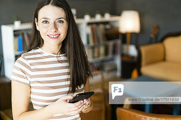 Glückliche Frau hält Smartphone in der Hand  während sie im Café steht
