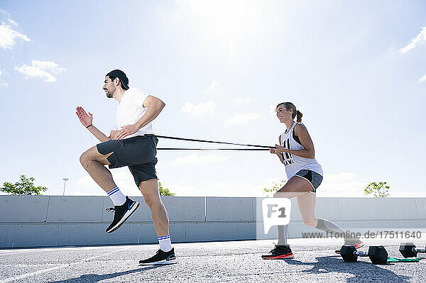 Couple exercising with strap on road against sky during sunny day