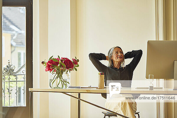 Businesswoman with hands behind head looking up at home office