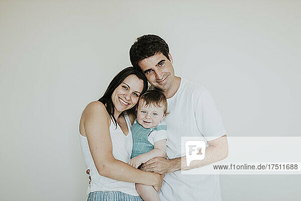 Parents carrying cute baby daughter while standing against white wall at home