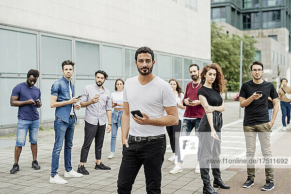 Group of friends using smart phones wile standing on footpath in city