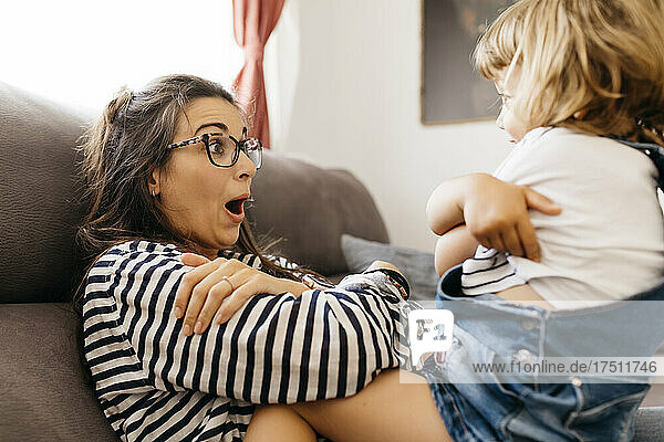Happy mother playing with daughter while sitting on sofa at home