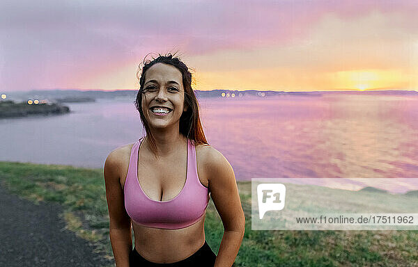 Smiling female athlete standing against sea during sunset