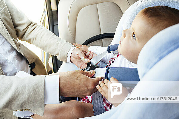 Father fastening baby boy sitting in child's seat in a car