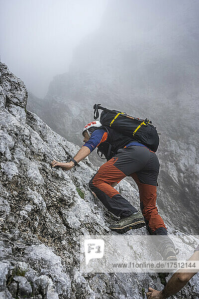 Mature male hiker climbing on mountain during foggy weather  Bergamasque Alps  Italy