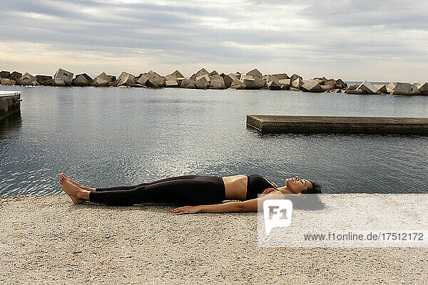 Mid adult woman lying on promenade by sea against cloudy sky in city