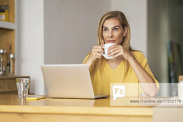 Thoughtful mature woman drinking coffee while sitting at table
