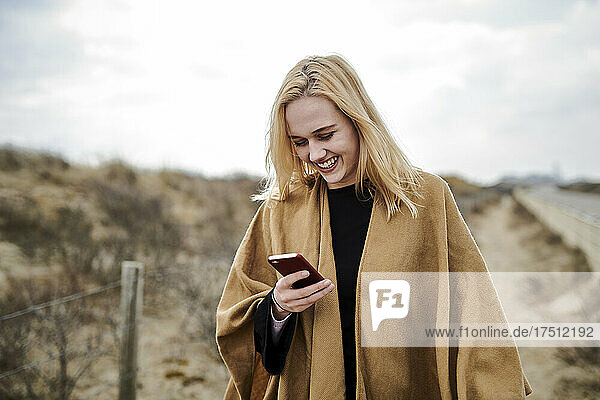Laughing young woman looking at smartphone on the beach