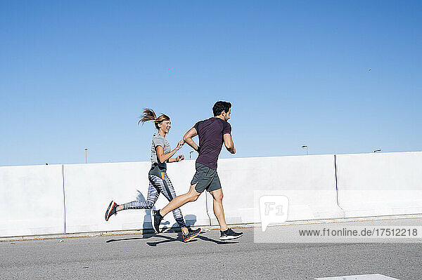 Couple running on road against clear blue sky in city during sunny day