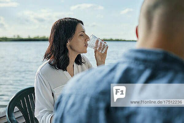 Young woman drinking glass of water at a lake