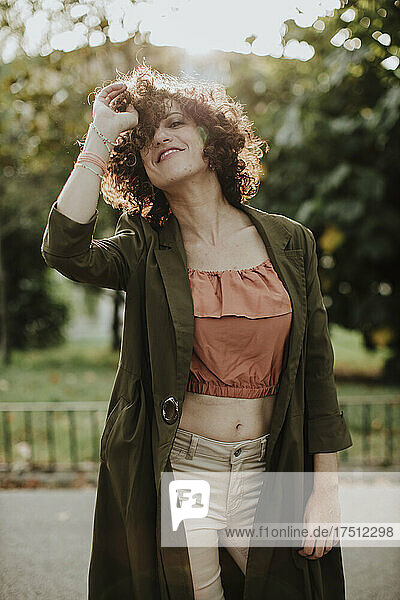 Smiling woman with curly hair wearing coat while standing in park