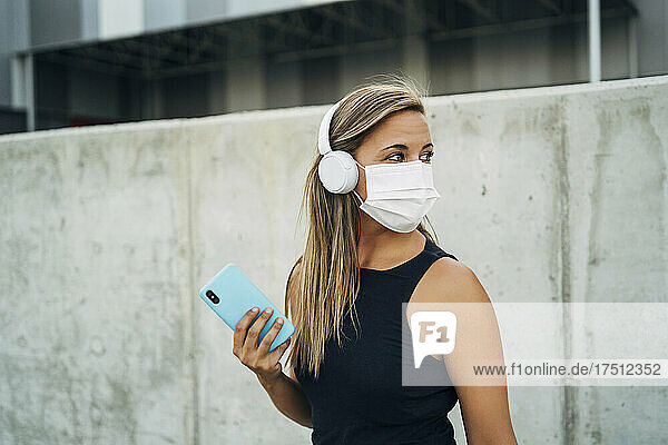 Young athletic woman with protective mask  headphones and smartphone