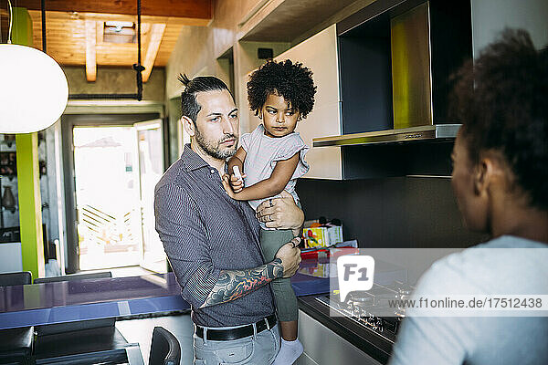 Vater trägt Tochter  während er zu Hause mit Frau in der Küche spricht
