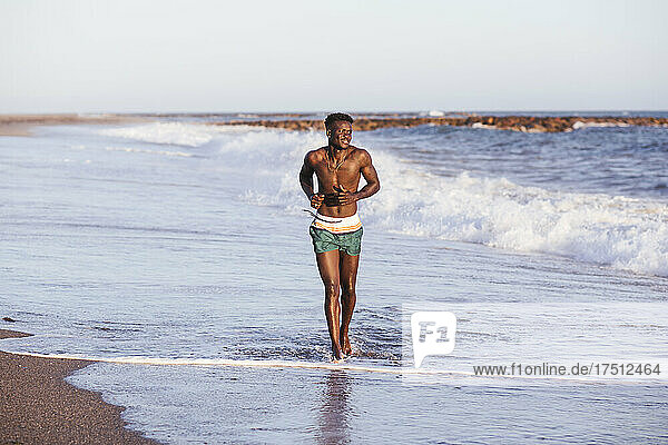 Shirtless African young man running at shore against clear sky