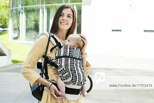 Smiling mother with her baby boy in baby carrier in city
