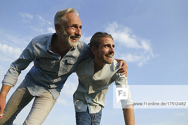 Carefree father with adult son under blue sky