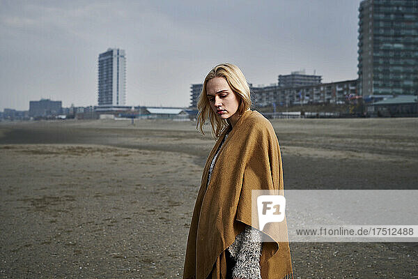 Netherlands  Zandvoort  portrait of blond young woman on the beach wearing light brown cape