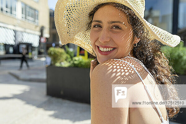Close-up of smiling beautiful woman wearing hat sitting in city on sunny day
