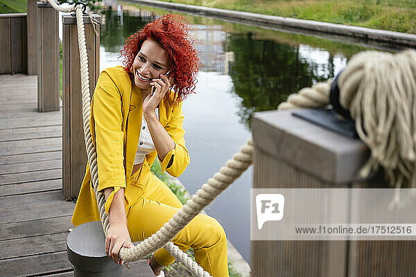 Young woman with curly hair and yellow suit sitting by the riverside  talking on the phone