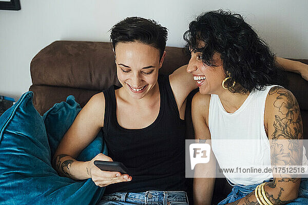 Cheerful woman looking at partner using phone on sofa