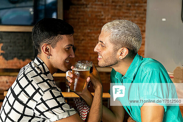 Romantic gay couple enjoying drinking beer with arm in arm at bar
