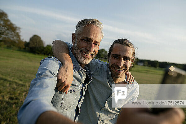 Happy father with adult son taking a selfie on a meadow in the countryside